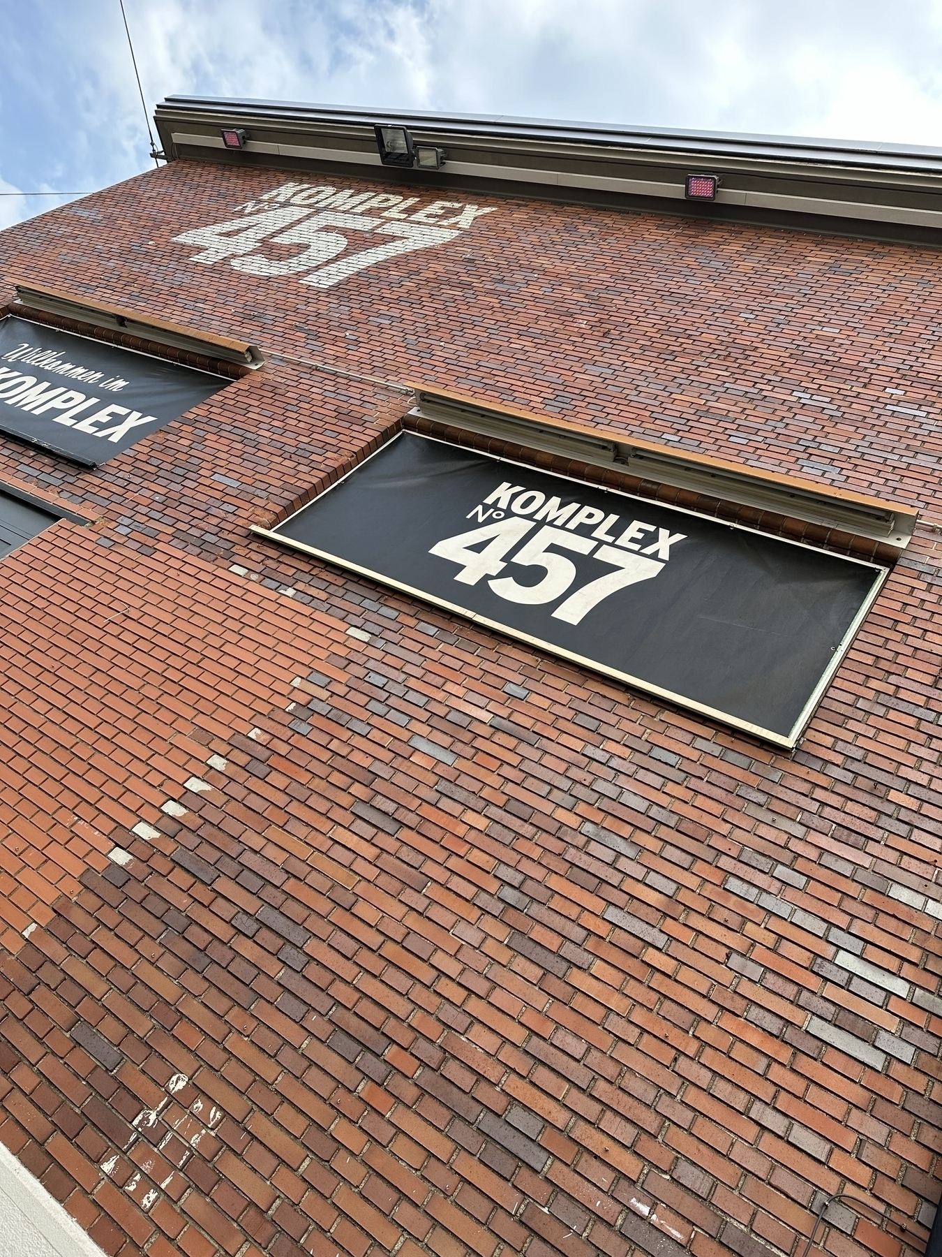 A brick building is shown with the text KOMPLEX 457 displayed on a large vertical sign and on window coverings.